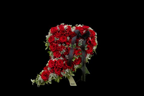 Ein herzförmiges Gesteck aus roten Rosen und grünem Blattwerk mit schwarzer Schleife.