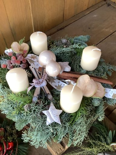 Adventskranz mit vier weißen Kerzen, Tannenzweigen und weihnachtlicher Dekoration.